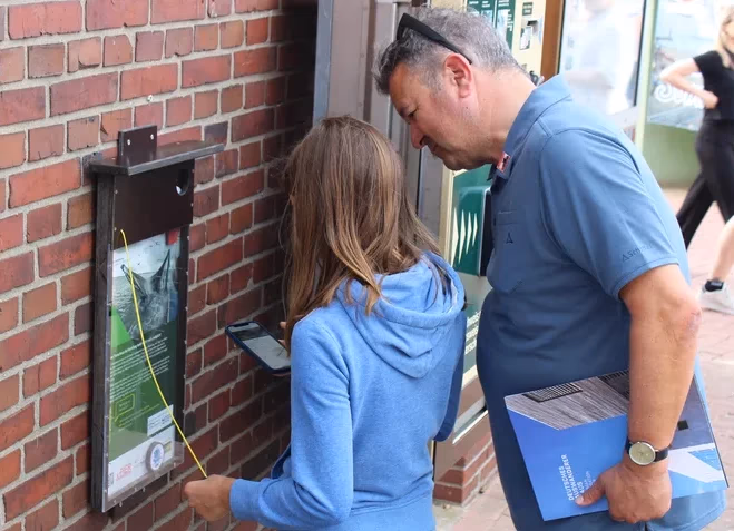 Manuel Andrack und ein Kind lösen an einer Backsteinwand eine Station der Bremerhavener Geocaching-Tour