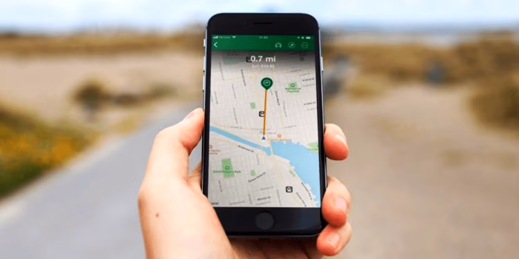 Hand hält auf einem Feldweg ein Smartphone mit geöffneter Geocaching-Karte