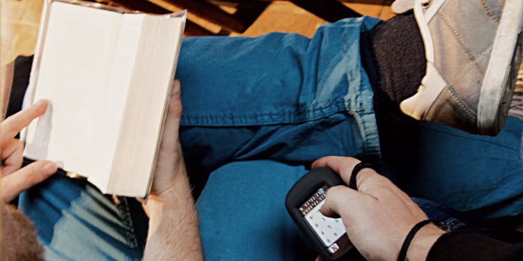 Person liest ein Buch und hält ein GPS-Gerät in der Hand