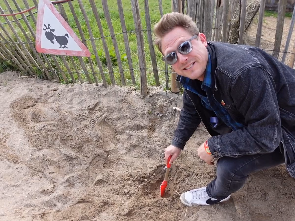 Der Geocaching Vlogger hockt lachend an einer Station im Karls Erlebnis-Dorf und gräbt im Sand nach dem nächsten Hinweis