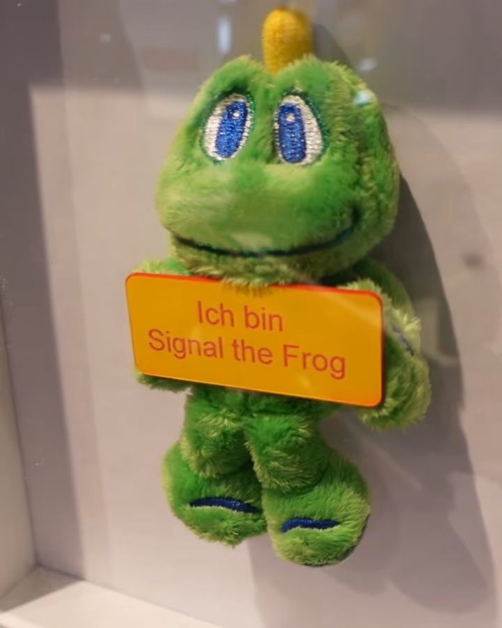 Signal the Frog, das Maskottchen von Geocaching, wartet in einer Vitrine