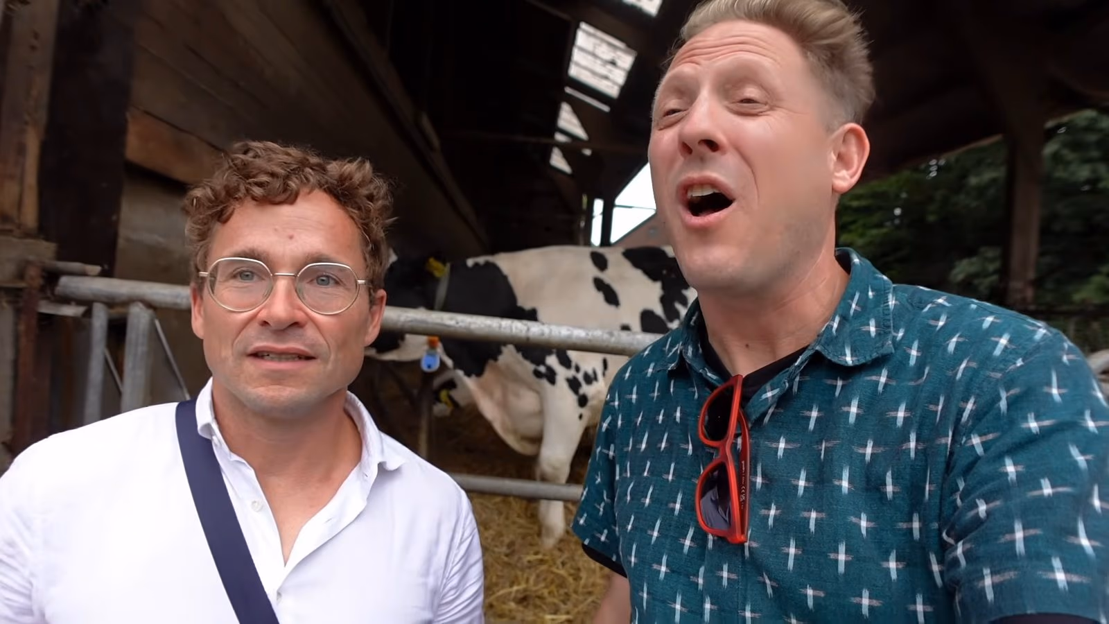Daniel Pflieger und der Geocaching Vlogger im Stall eines Milchviehbetriebs, hinter ihnen eine Kuh