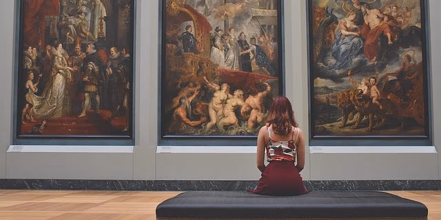 Frau sitzt auf einer Bank vor großformatigen Gemälden in einem Museum