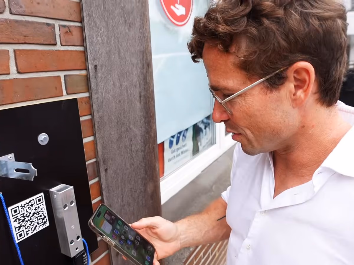 Daniel Pflieger schaut an einer Station der Milchland GeoTour auf sein Handy, links der QR-Code der Station