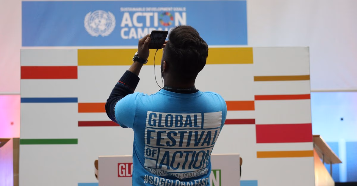 Mann im T-Shirt „Global Festival of Action“ fotografiert eine Wand der UN-Aktionskampagne zu den Nachhaltigkeitszielen