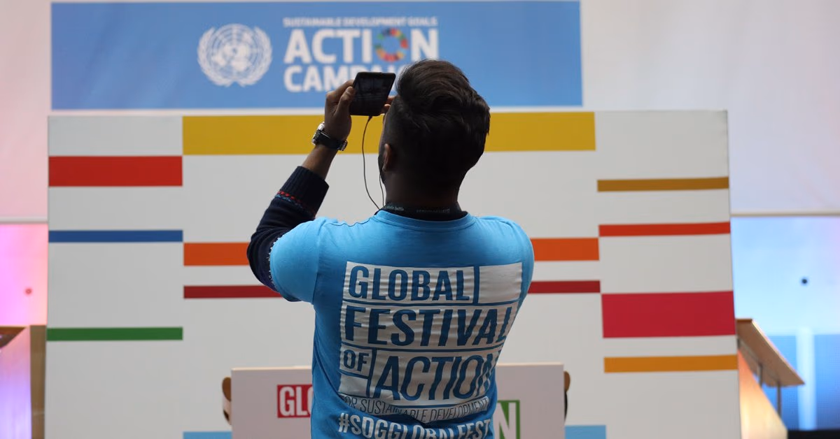 Mann im T-Shirt „Global Festival of Action“ fotografiert eine Wand der UN-Aktionskampagne zu den Nachhaltigkeitszielen
