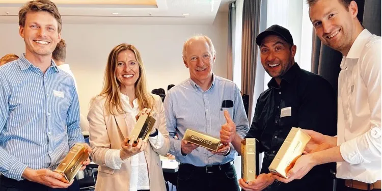 Fünf Teilnehmende eines Team-Events halten lachend goldfarbene Barren in die Kamera