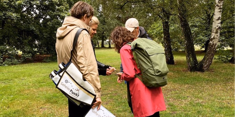 Drei Menschen mit Rucksäcken schauen in einem Park gemeinsam auf ein Smartphone
