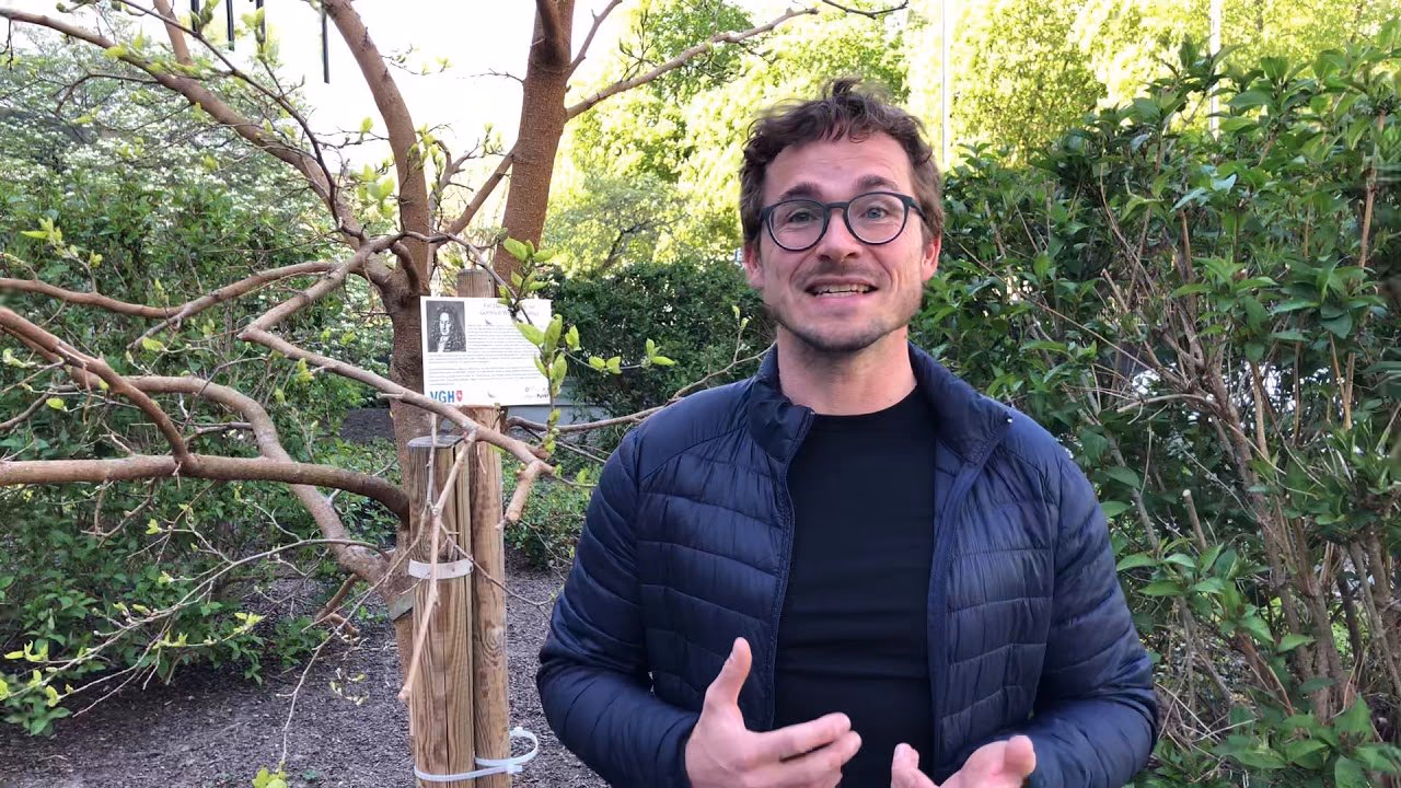 Daniel Pflieger steht zwischen Bäumen und erklärt etwas in die Kamera